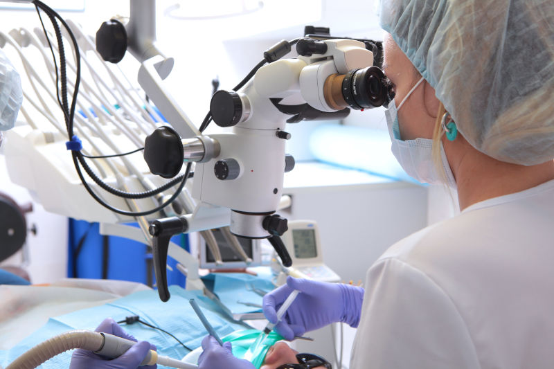 A dentist performing a complex procedure on a patient with the help of a microscope.